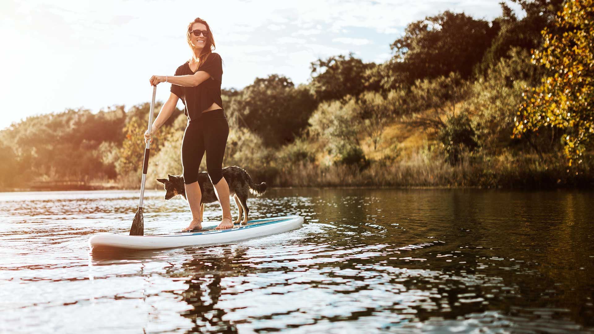 A woman on a paddle board with her dog.