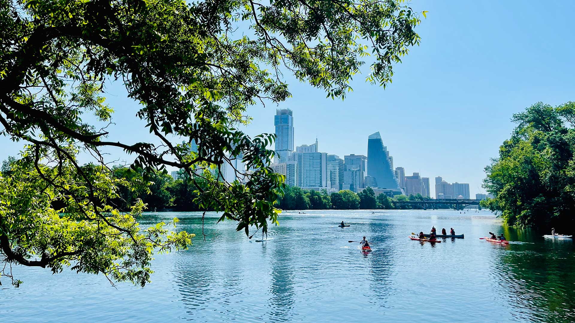 People canoeing in the Colorado River with the Austin skyline in the background.